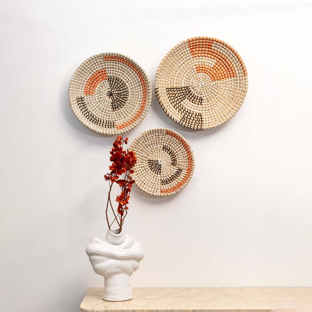 Grouped boho woven wall baskets displayed above a light wood console table with a ceramic vase for living room styling.