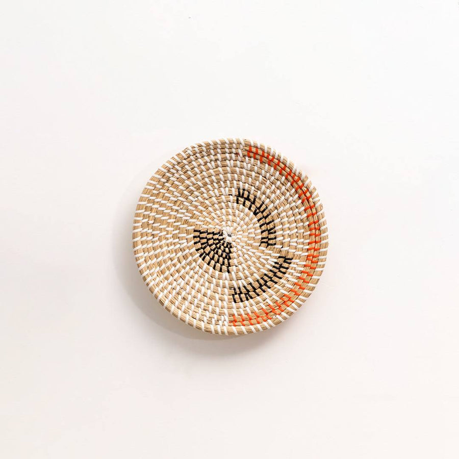 Round handwoven seagrass wall basket with black and rust patterns for bohemian living room accent on a white background.