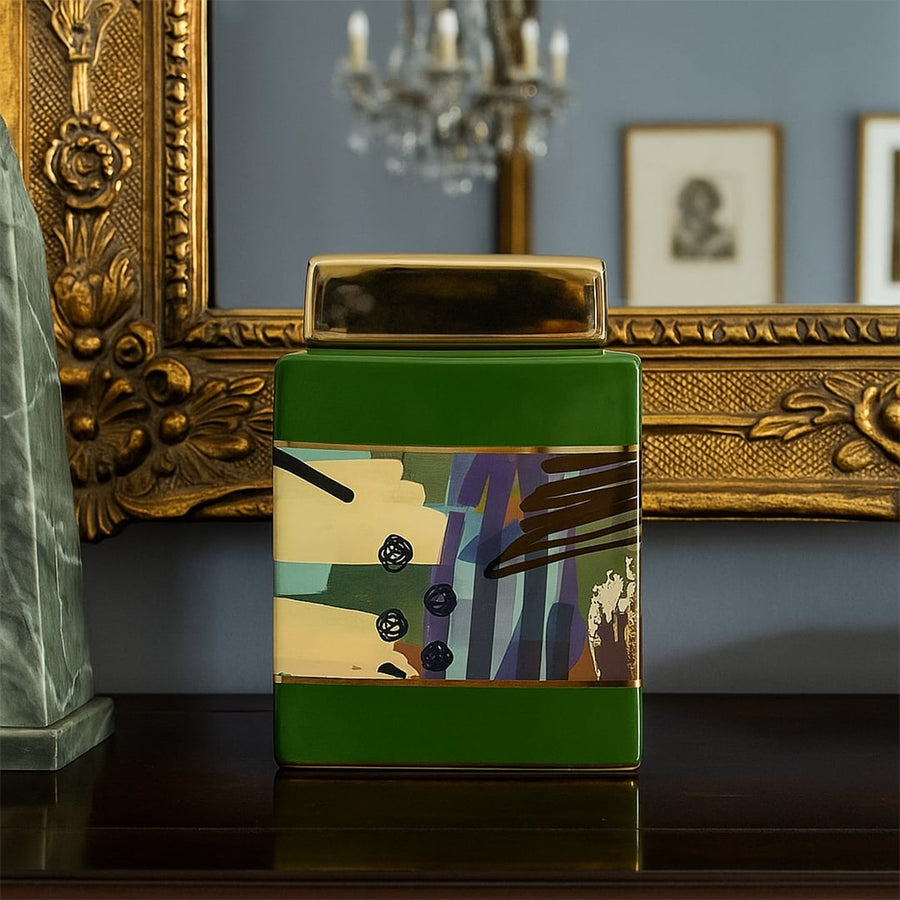 Green ceramic decor jar with abstract multicolor artwork and gold lid placed on dark console before ornate framed mirror adding luxe home styling.