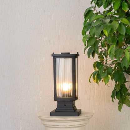 Black outdoor pillar lamp with frosted glass panel showing bright LED bulb and durable square metal frame.