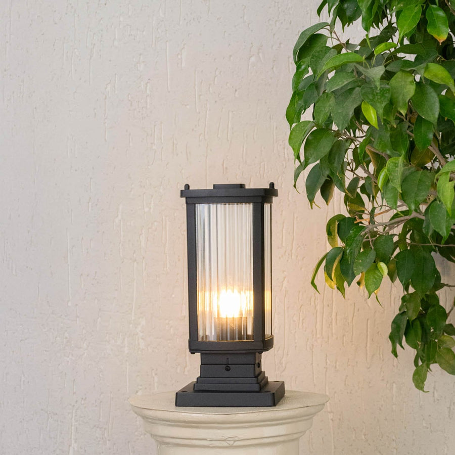 Black outdoor pillar lamp with frosted glass panel showing bright LED bulb and durable square metal frame.