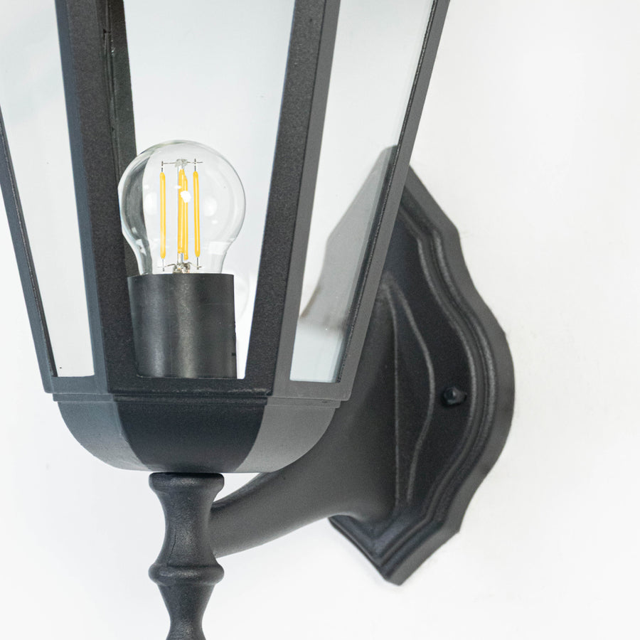 Closeup image of black metal outdoor wall light with clear glass shade for elegant exterior lighting decor.