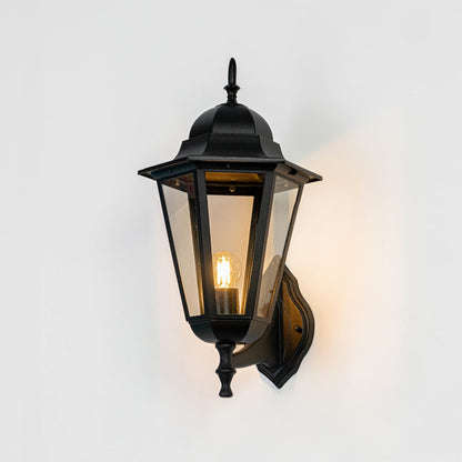 Black metal and clear glass outdoor wall lantern mounted on exterior wall creating warm entryway lighting ambiance shown Light on white BG.