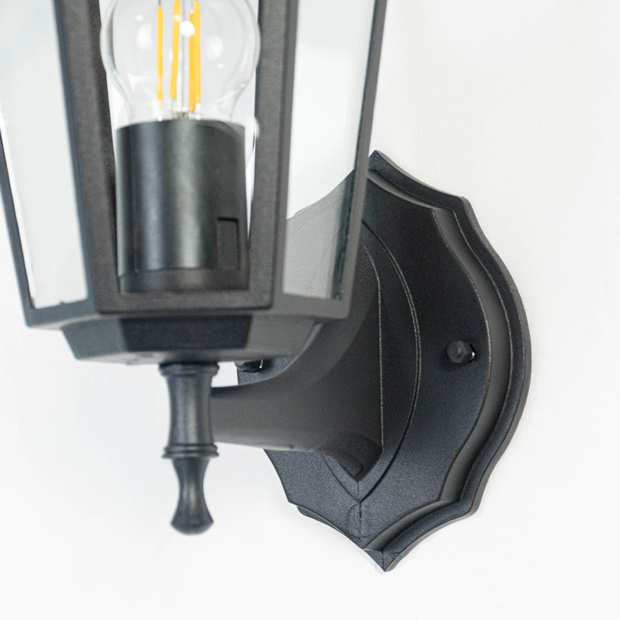 Closeup image of black metal outdoor wall light with clear glass shade for elegant exterior lighting decor.