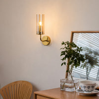 Contemporary gold brass single candle wall sconce with a clear glass cylinder tube shade styled in a cozy dining room.