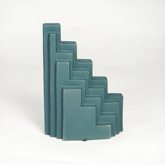 Teal ceramic stepped decorative sculpture with layered angular design isolated on white background for contemporary home decor use.
