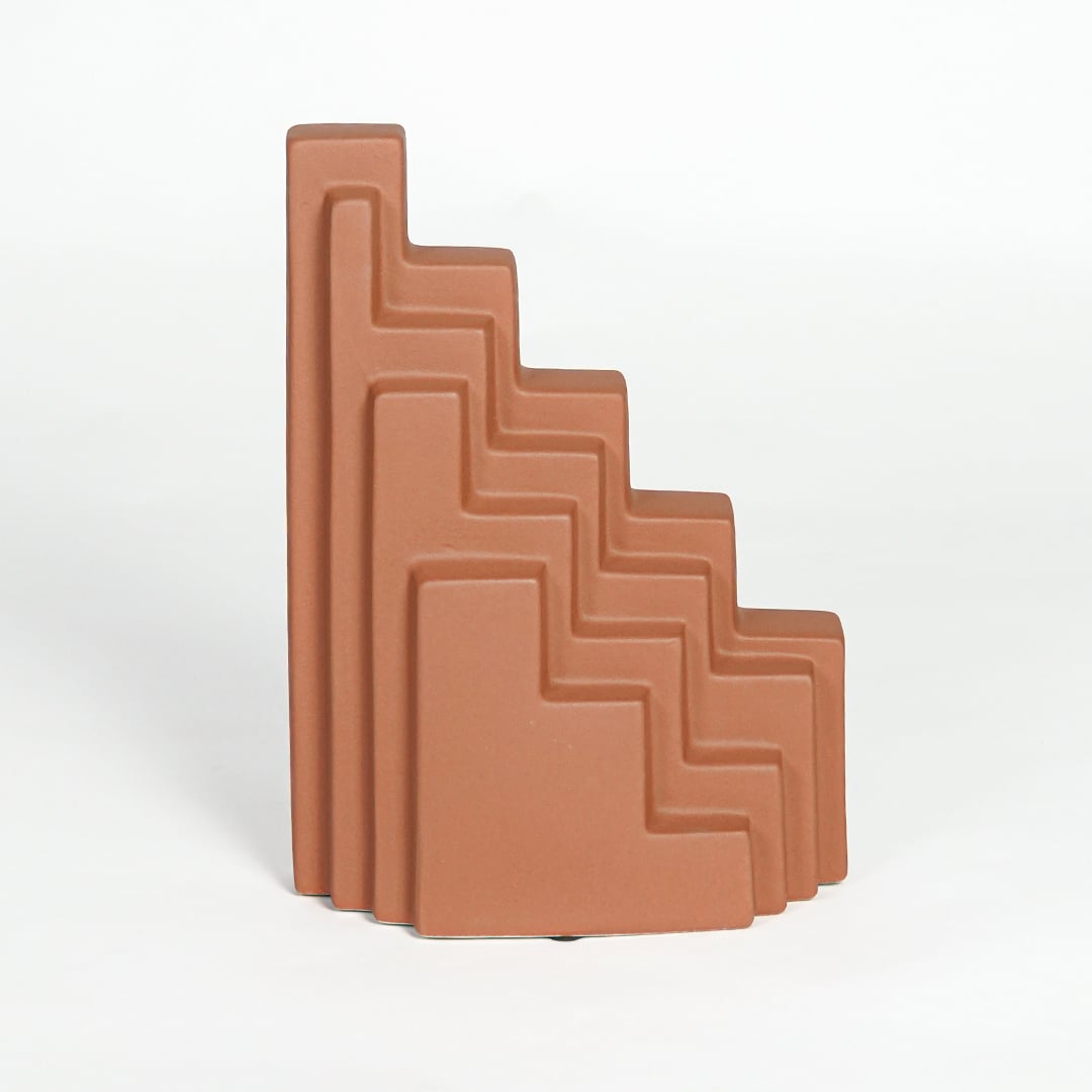 Orange ceramic stepped decorative sculpture with geometric layered design isolated on clean white background for contemporary decor display.