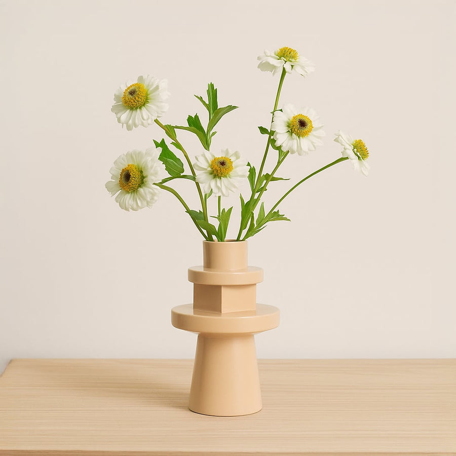 Modern beige ceramic geometric vase holding white daisy flowers on a light wooden table for minimalist Scandinavian home decor styling.