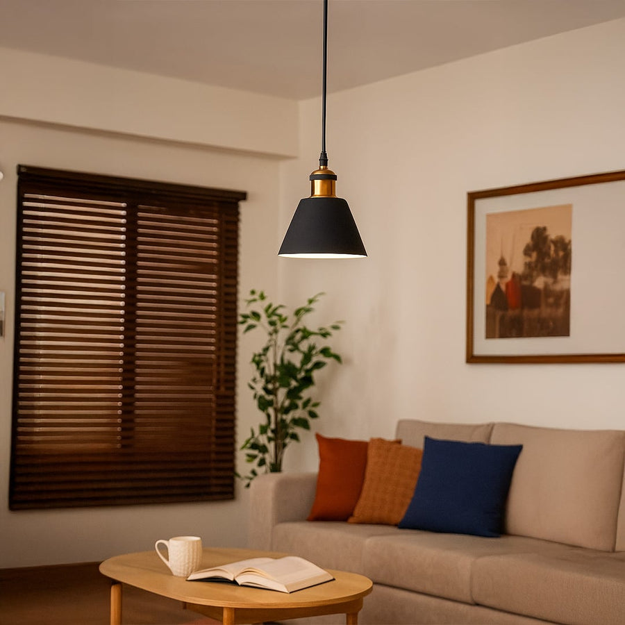 Black cone pendant light glowing warmly above a wooden coffee table in a cozy modern living room with a beige sofa and colorful cushions.