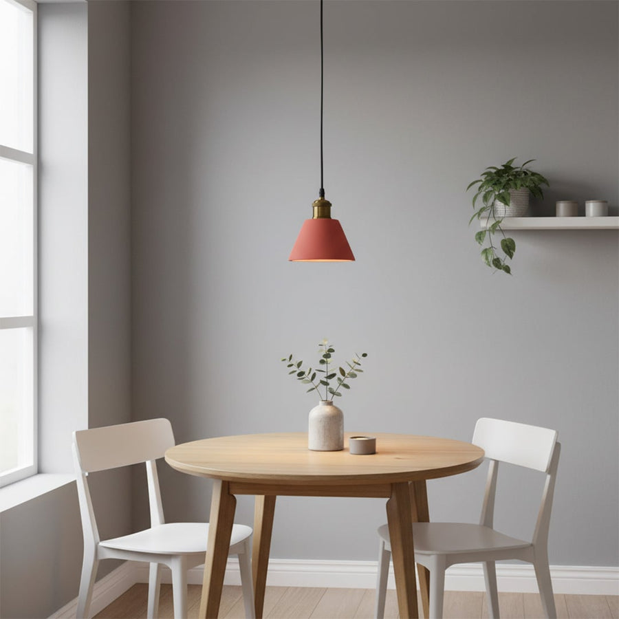 Terracotta cone pendant light glowing softly above a round wooden dining table with a small vase and two white chairs.