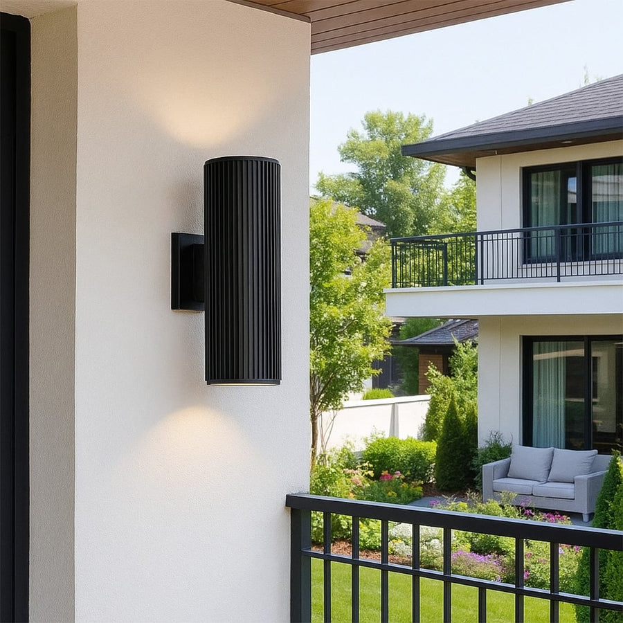 Tall black cylindrical wall light illuminating a modern entryway with elegant glow and contemporary architectural appeal.