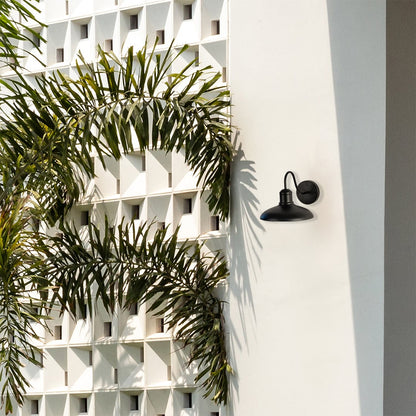 Matte black metal outdoor wall light mounted on a white exterior wall with lush greenery adding stylish outdoor illumination to modern homes.