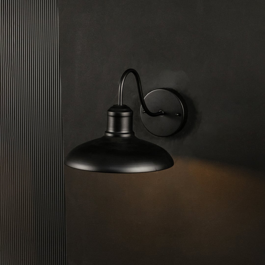 Matte black outdoor wall sconce shown glowing on a black background enhancing its warm light and modern industrial look.