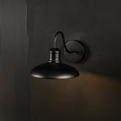 Matte black outdoor wall sconce shown glowing on a black background enhancing its warm light and modern industrial look.
