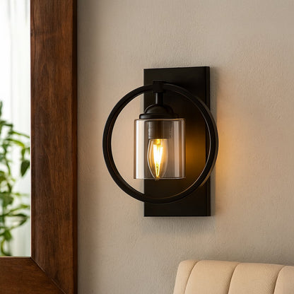 Wall light in black metal with glass shade mounted beside sofa adding warm ambient glow and modern accent to living room decor.