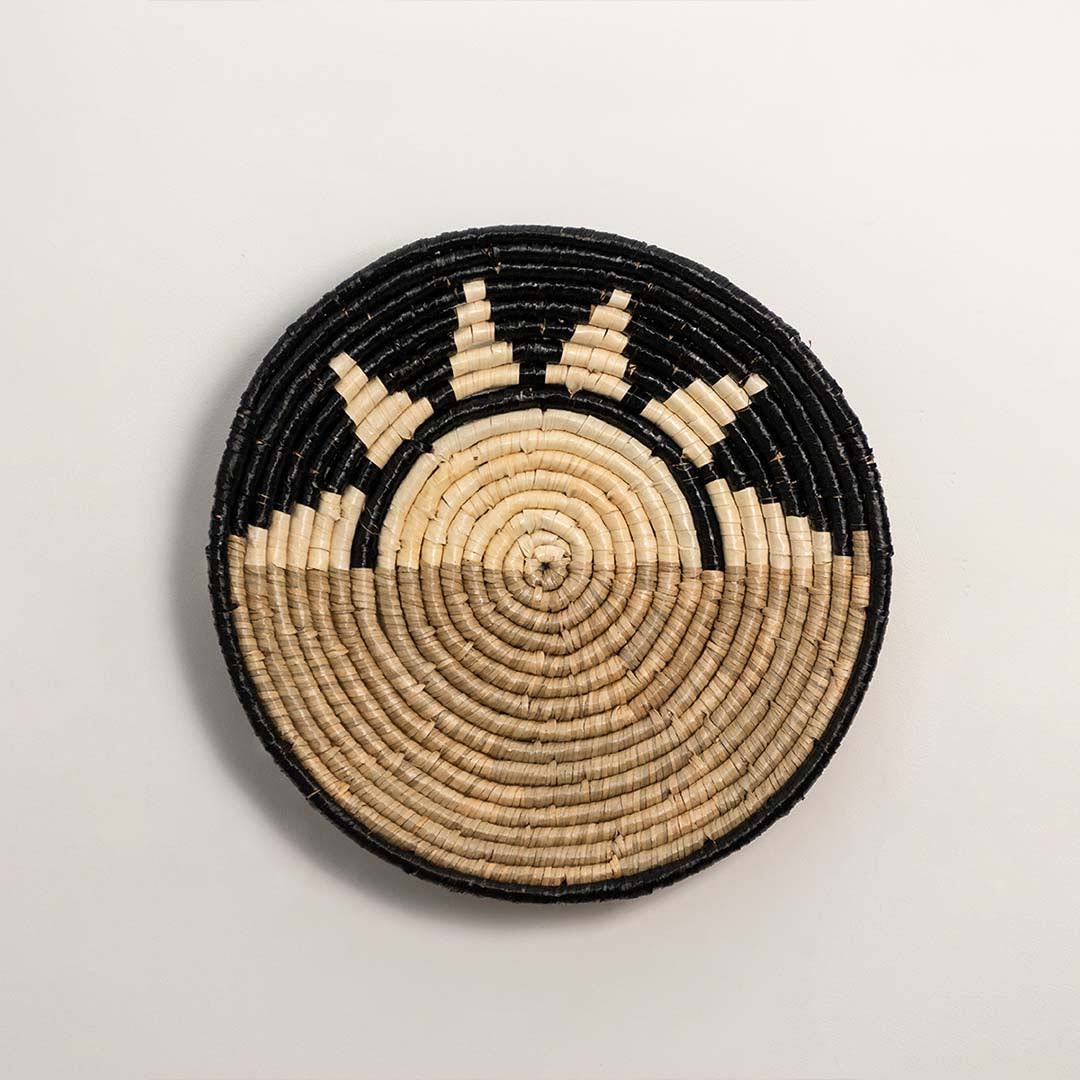 Round handcrafted black and natural seagrass wall basket with sunrise pattern on white background image.