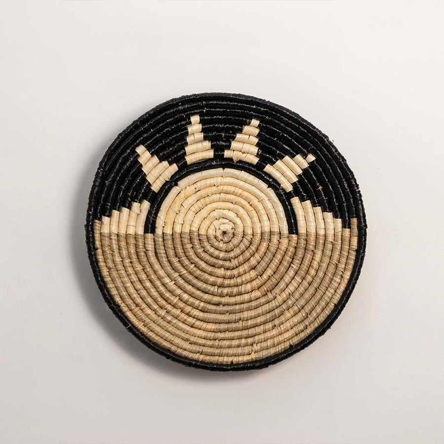 Round handcrafted black and natural seagrass wall basket with sunrise pattern on white background image.