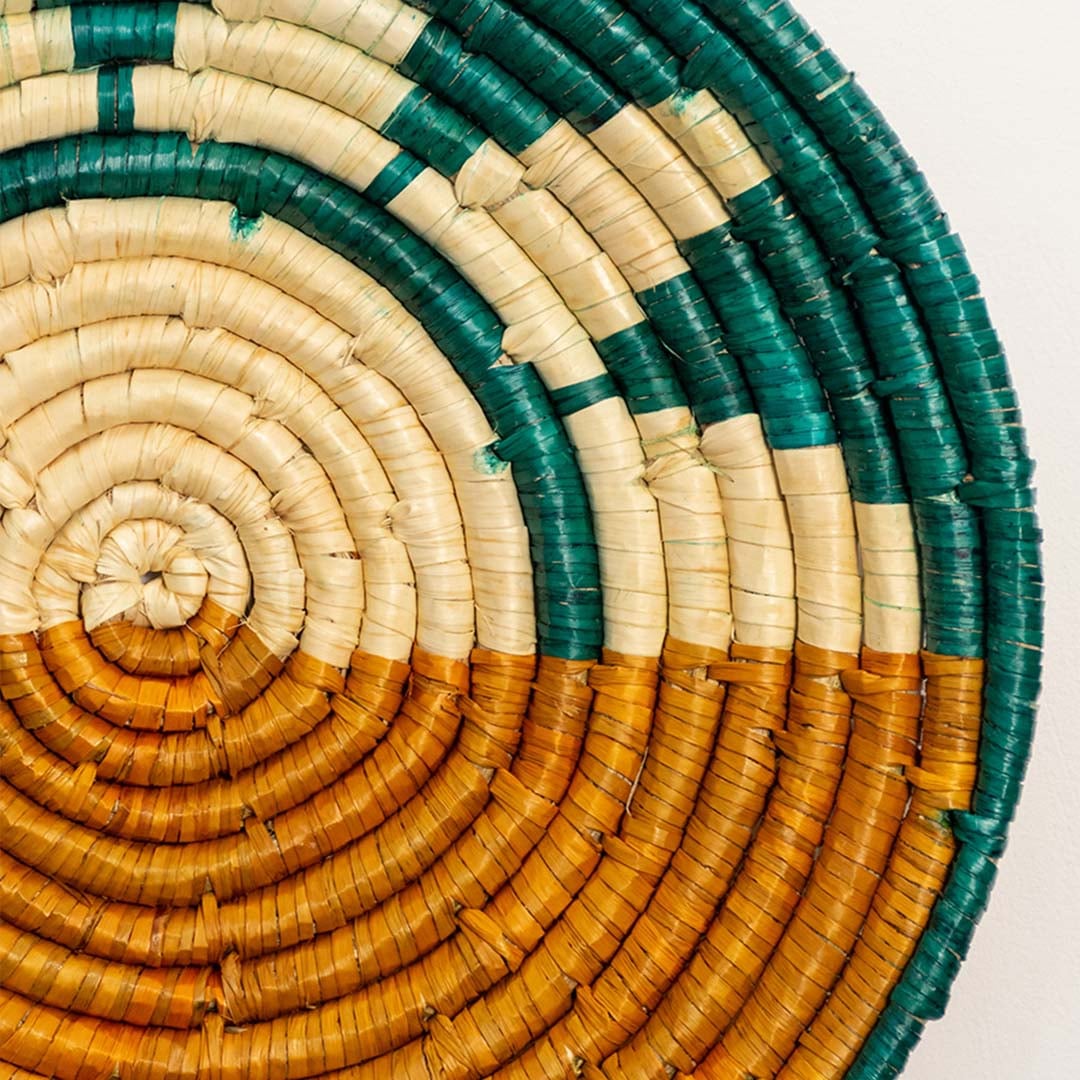 A closeup view of the teal mustard and natural rattan wall decor plate showing its intricate sunburst weave and handcrafted textured design for vibrant earthy decor styling.