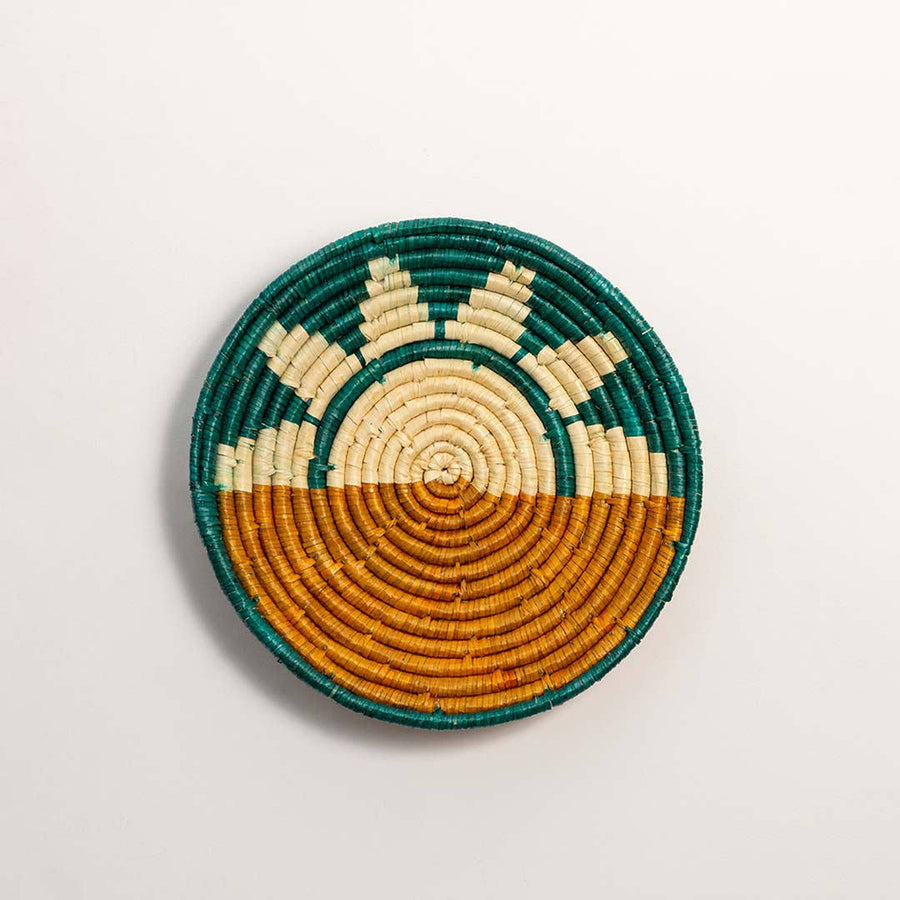 Round woven teal and brown sunrise pattern seagrass wall basket hanging display on white background image.