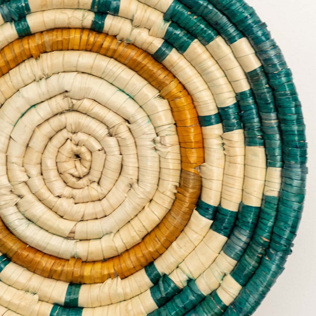 A closeup view of the teal mustard and natural rattan wall decor plate showing its detailed sunburst inspired weave and textured handcrafted pattern for vibrant decor styling.