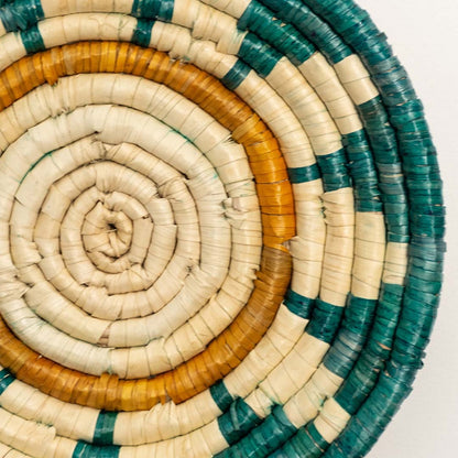 A closeup view of the teal mustard and natural rattan wall decor plate showing its detailed sunburst inspired weave and textured handcrafted pattern for vibrant decor styling.