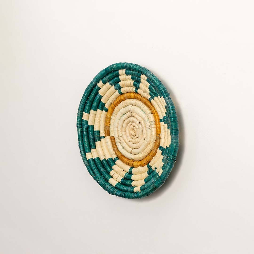 Side view of handcrafted teal seagrass wall basket with woven sunrise pattern for artisan boho home décor.