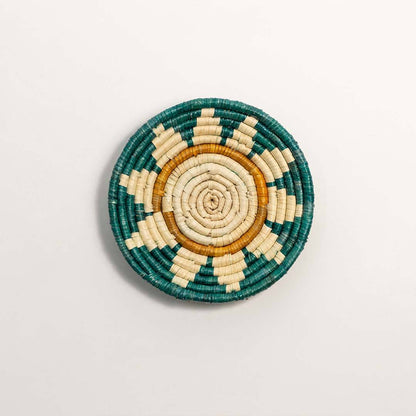 Round handcrafted teal and natural seagrass wall basket with sunrise pattern on white background image.
