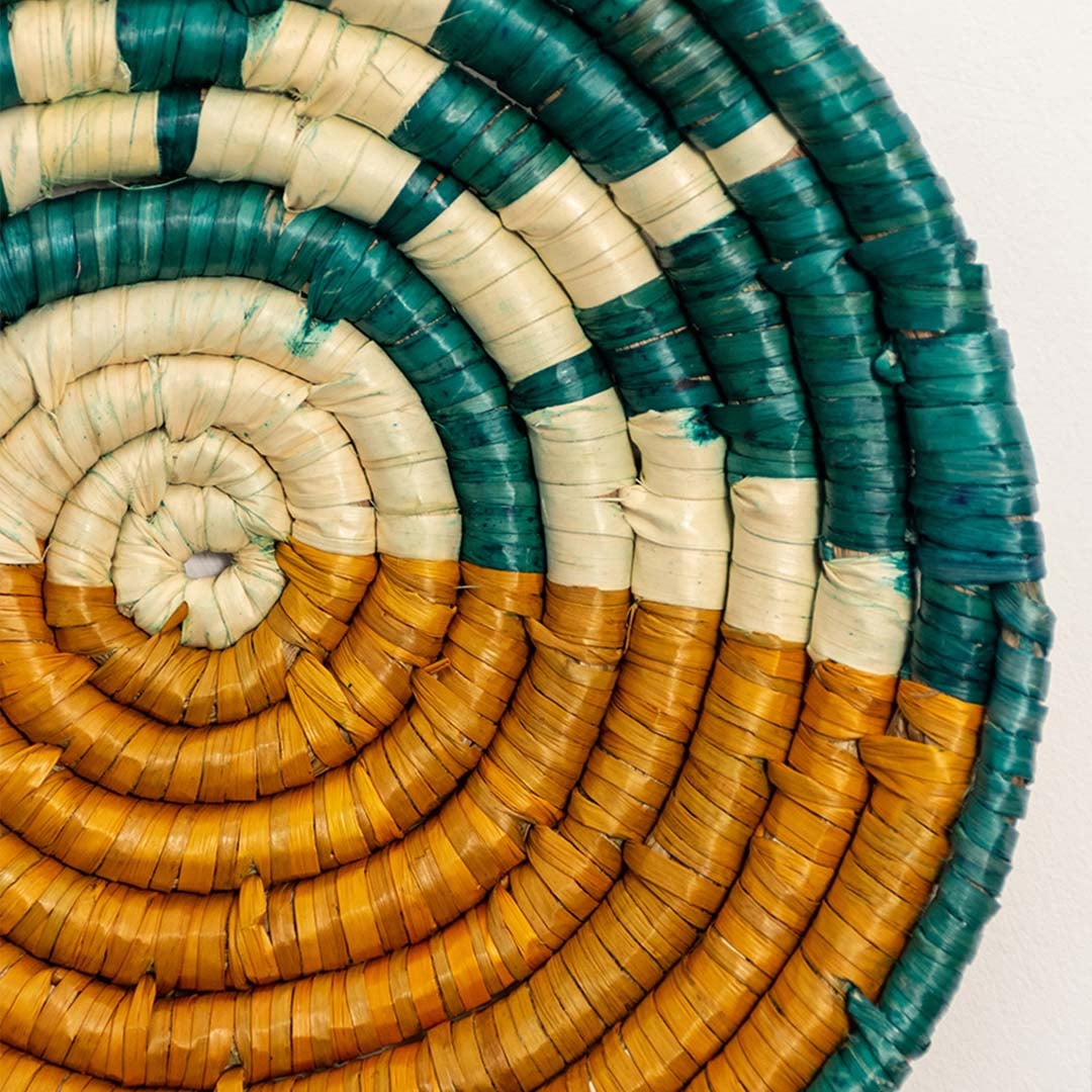 Detailed closeup view of the tight coil weaving and painted teal and yellow sections on the natural seagrass wall basket surface quality.