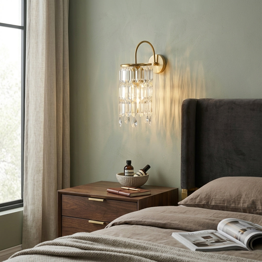 Gold crystal wall light installed above bed on soft beige wall background adding warm ambient lighting to modern bedroom interior.