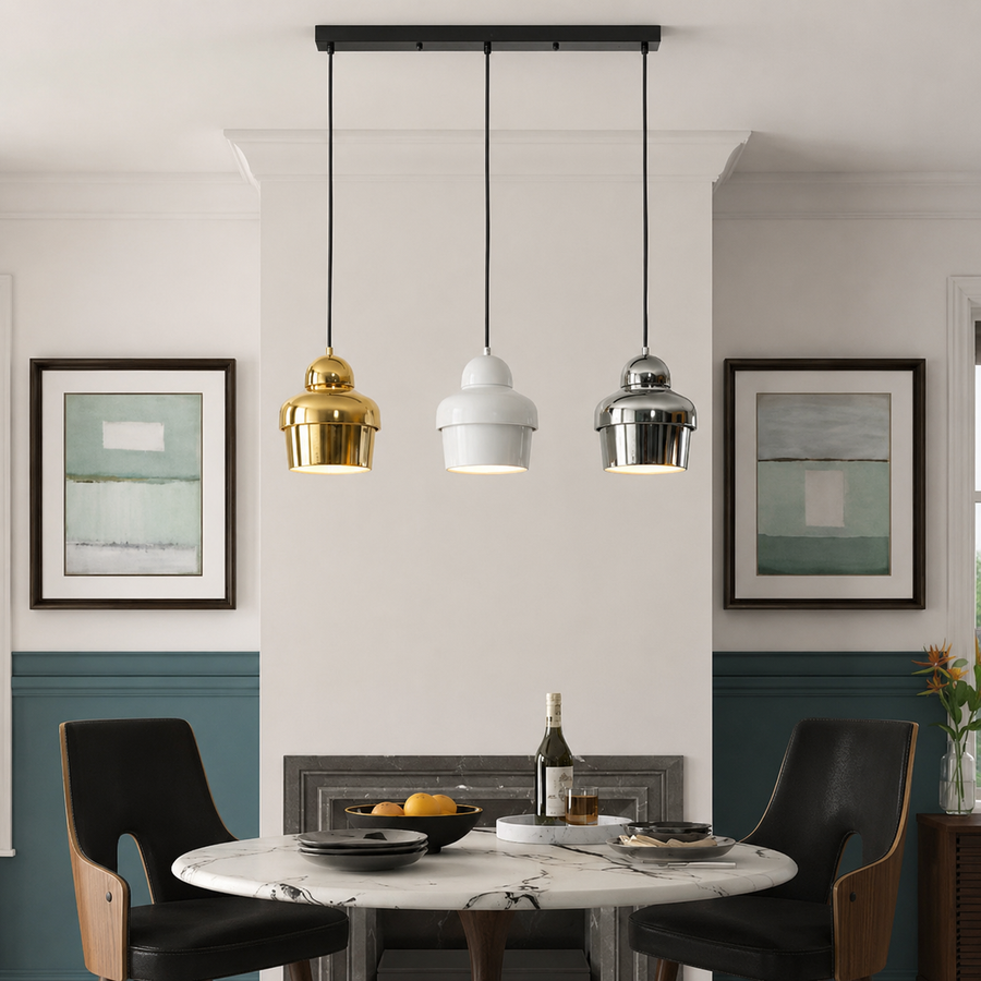 Three modern pendant lights in gold, white, and silver finishes hanging over a dining table in a styled interior room.