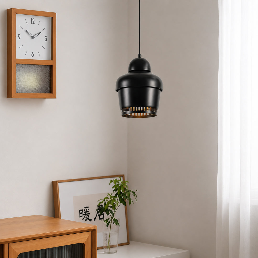 A modern black pendant light with a textured glass shade hangs in a minimalist room corner next to a wooden wall clock and a small potted plant.