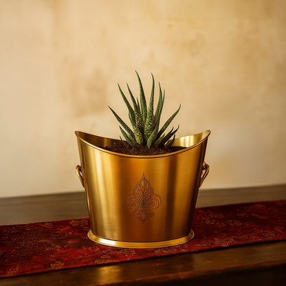 A gold planter bucket holding a green plant displayed on the top of a wooden table next to a in interior lifestyle scene.