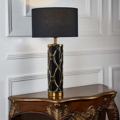 Black ceramic table lamp with black fabric shade and gold accents creating sophisticated luxury ambient lighting indoors.