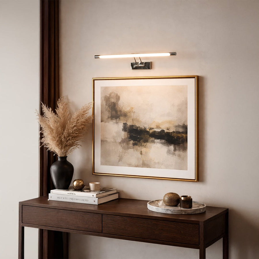 Gold metal picture light illuminating framed artwork above console table creating elegant gallery inspired interior decor.