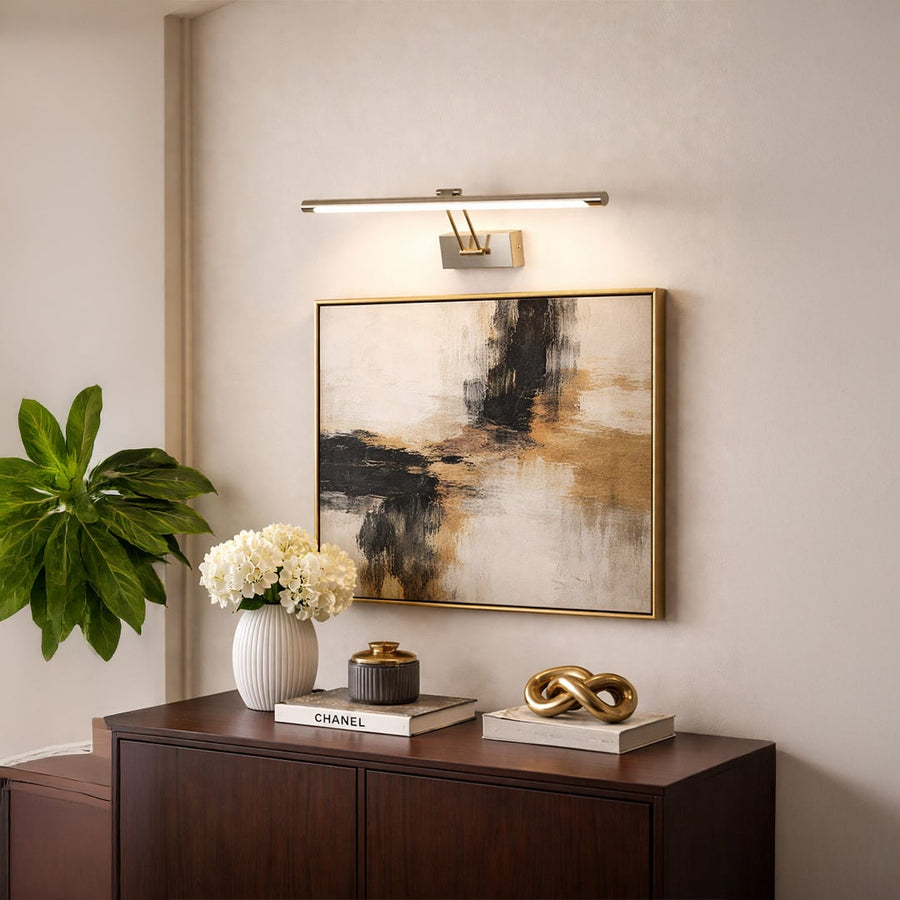 Gold metal picture light enhancing abstract wall art with warm illumination above console table in modern interiors.