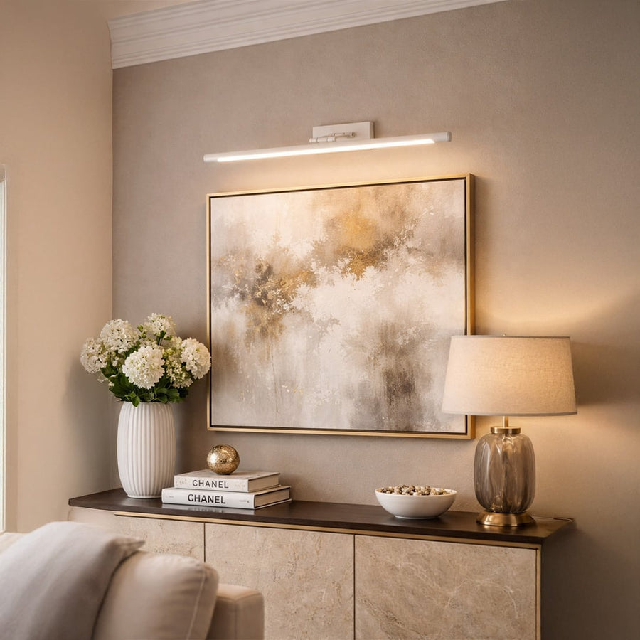 Gold metal picture light enhancing framed artwork with warm focused illumination in a sophisticated bedroom setting.