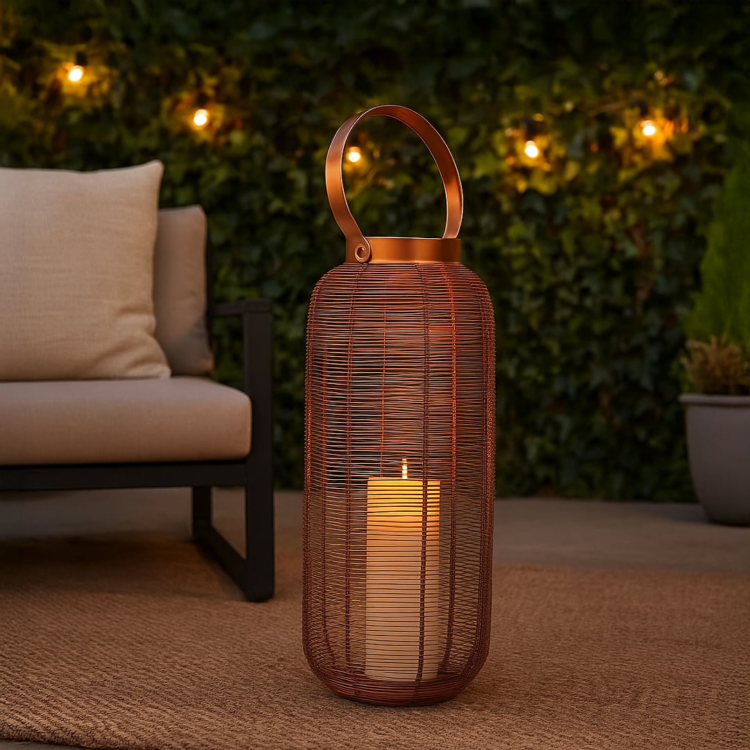 Elegant copper wire lantern with illuminated LED candle creating a warm glow on an outdoor patio rug next to a modern sofa for evening ambiance.