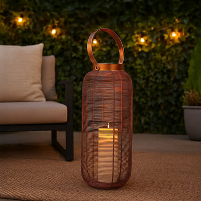 Elegant copper wire lantern with illuminated LED candle creating a warm glow on an outdoor patio rug next to a modern sofa for evening ambiance.