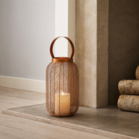 Boho woven rattan textured wire cage floor lantern with a copper metal handle and a large pillar candle sitting next to a fireplace.