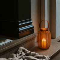 Boho woven rattan textured wire cage floor lantern with a copper metal handle sitting on a stone step next to a black architectural pillar.