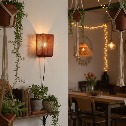 Boho style rectangular red woven wall sconce casting a warm glow next to indoor plants and a wooden dining room table setting.