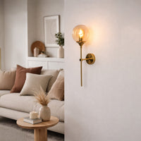 Elegant brass wall light with clear glass globe creating warm cozy living room interior ambiance.