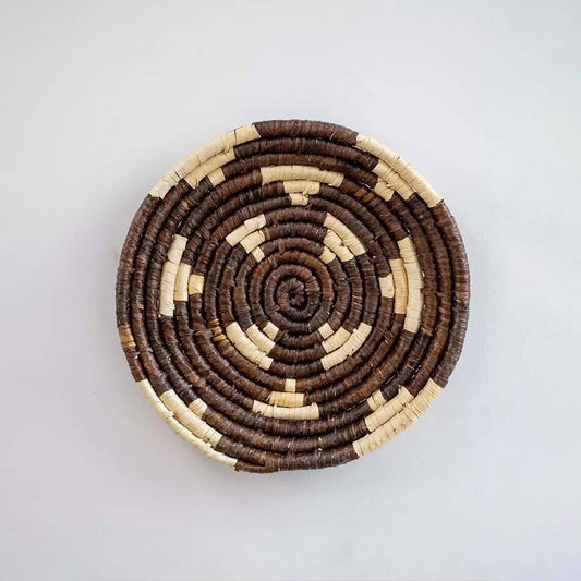 Handwoven seagrass round wall basket decor in natural beige and dark brown with spiral woven pattern on white background.