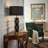 Table lamp with black fabric shade and metal base placed on side table adding rich ambient lighting to luxurious living room interior.