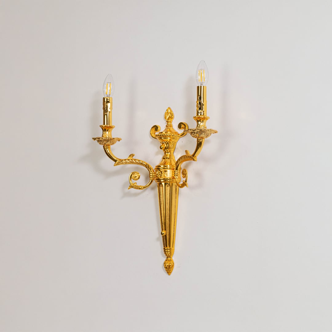 Golden wall light with candle style bulbs elegant wall mounted decorative lighting piece on off white background.