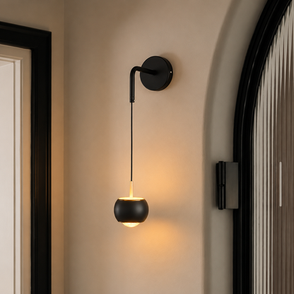 A modern black wall-mounted sconce with a spherical shade, shown lit in a warm glow on a beige wall between dark-framed doorways.