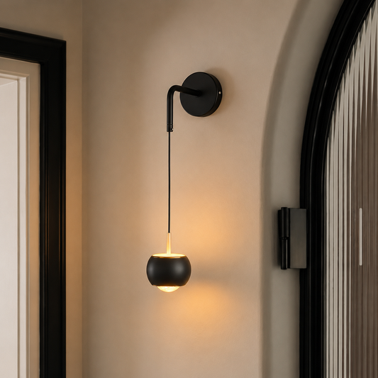 A modern black wall-mounted sconce with a spherical shade, shown lit in a warm glow on a beige wall between dark-framed doorways.