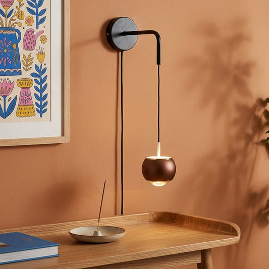 Minimalist black plug-in hanging wall sconce light with a small dark wood walnut bowl shade over a wooden console desk.