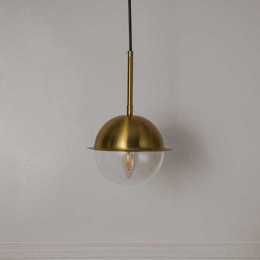 Brass metal pendant light with clear bulb and dome shade crafted for elegant modern interiors.