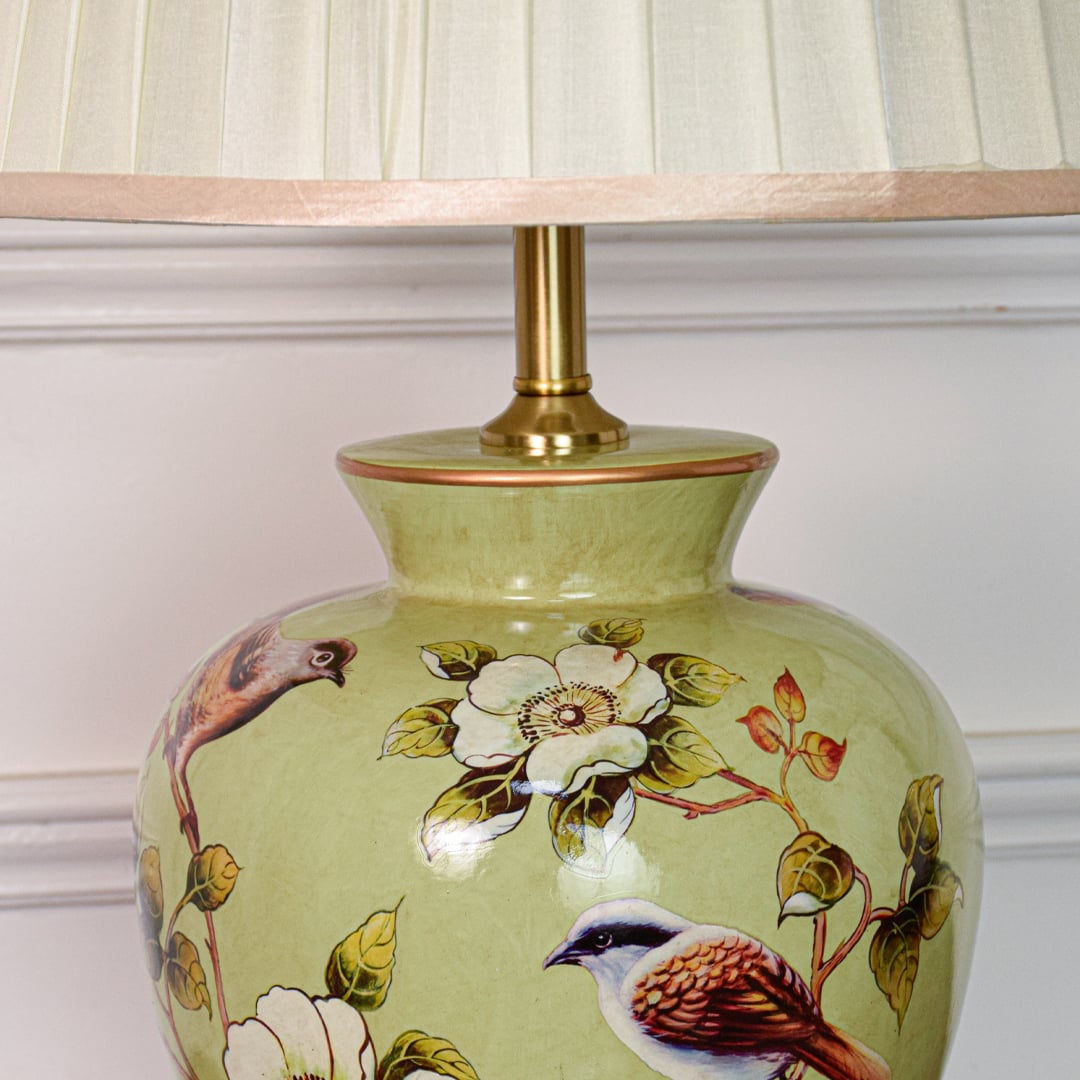 Closeup of green ceramic table lamp highlighting hand painted birds floral motifs smooth glaze finish and brass base.